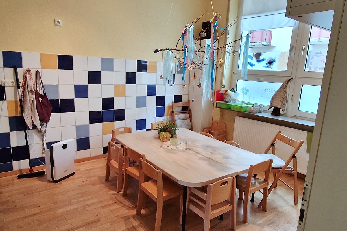Frühstückszimmer mit großem Tisch und Kinderstühlen am Fenster.
