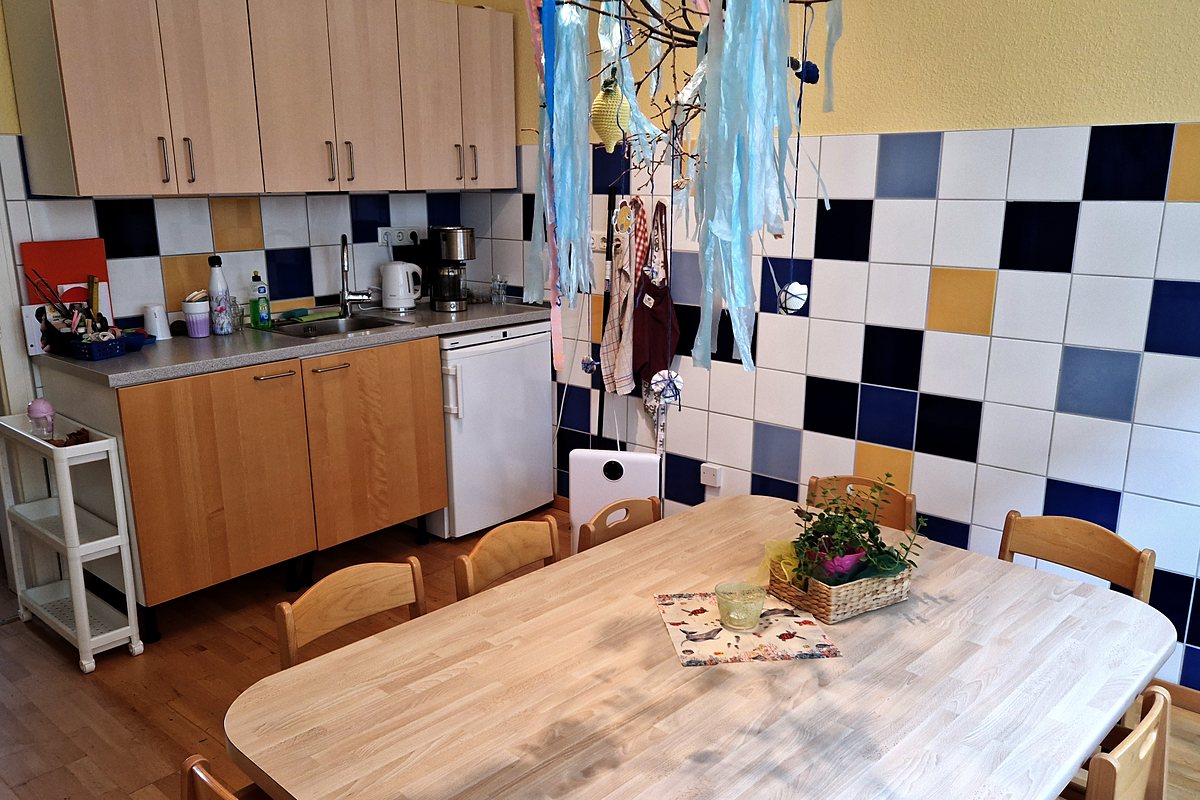 Küchenzeile mit Spüle, Kühlschrank und Kaffeemaschine neben dem großen Tisch.