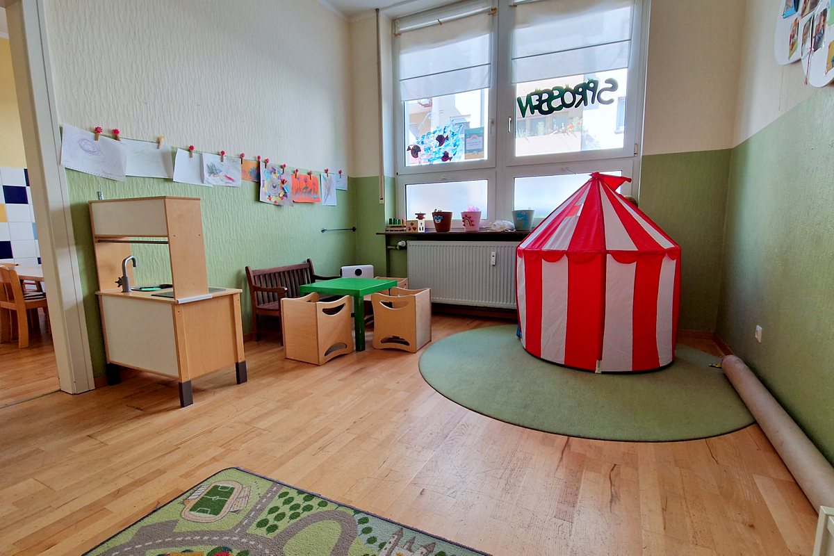 Spielezimmer mit großem Spielteppich, Kinderküche aus Holz und rot-weißem Spielzelt.