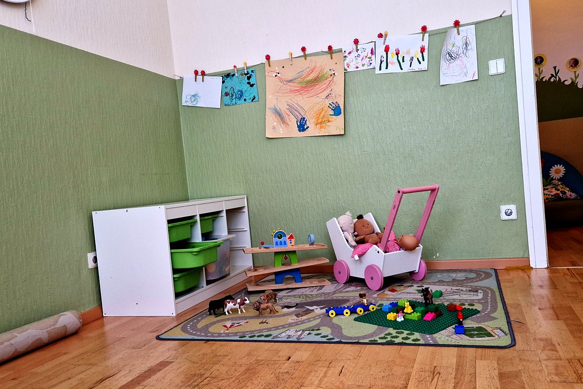 Spielecke mit niedrigem Regal, Puppenwagen und einer Leine mit Kinderzeichnungen.