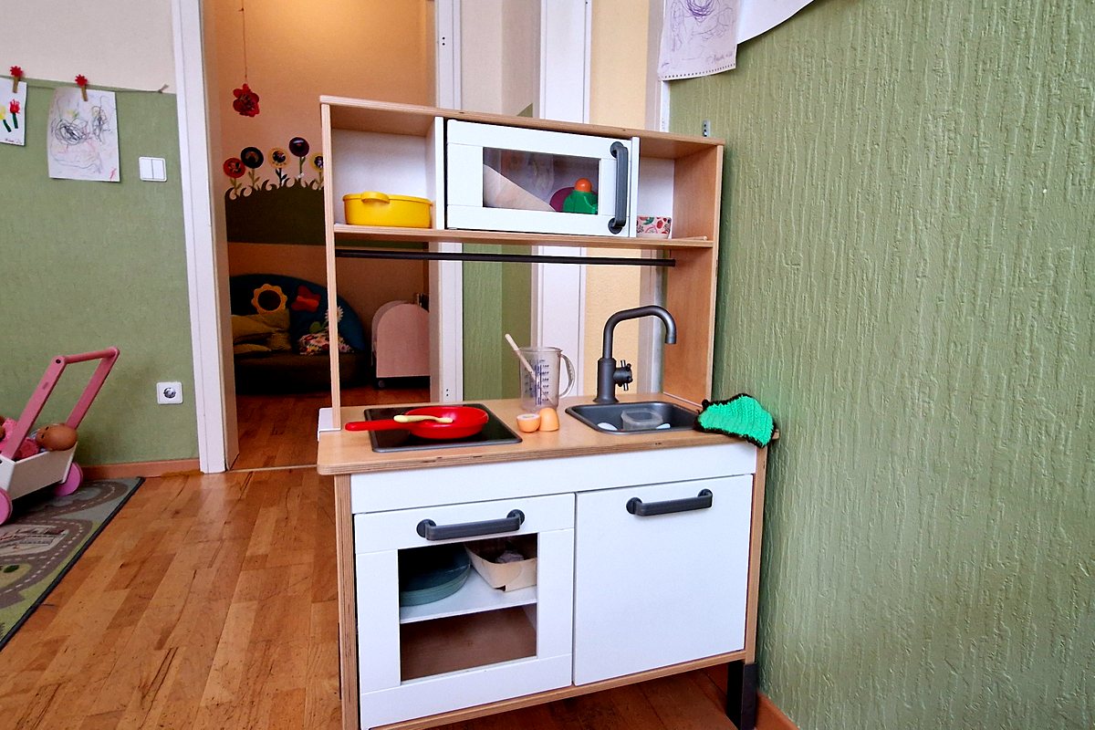 Kinderküche mit Spielgeschirr, daneben der offene Durchgang zum Nebenraum.